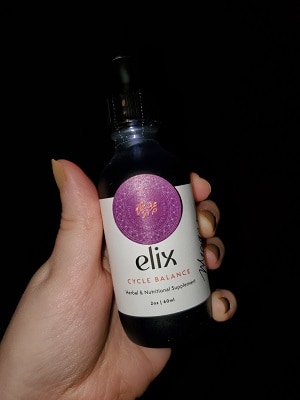 White female hand holding up bottle of elix cycle balance herbal supplement