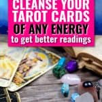 There are tarot cards and various crystals on a gray wood table. There is text in a pink box that says how to cleanse your tarot cards of any energy to get better readings