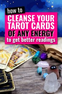 There are tarot cards and various crystals on a gray wood table. There is text in a pink box that says how to cleanse your tarot cards of any energy to get better readings